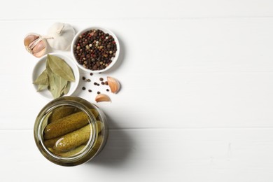 Tasty pickled cucumbers in jar and ingredients on white wooden table, flat lay. Space for text