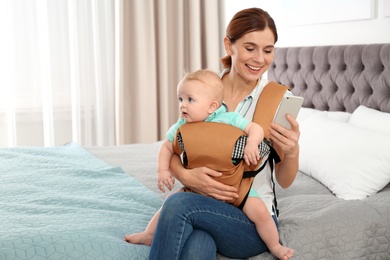 Photo of Woman with her son in baby carrier using smartphone at home