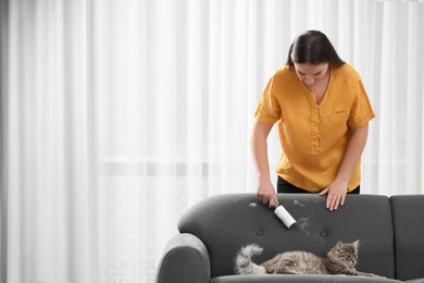 Photo of Pet shedding. Woman with lint roller removing cat`s hair from sofa at home, space for text