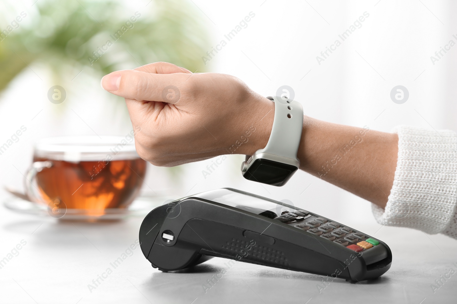 Photo of Woman using terminal for contactless payment with smart watch at table, closeup