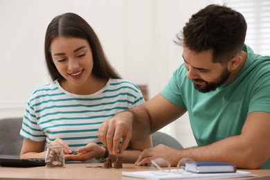 Happy young couple counting money at wooden table indoors