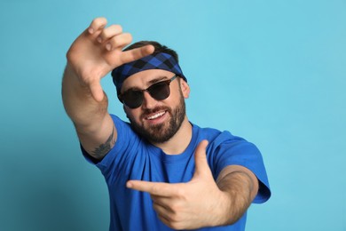 Fashionable young man in stylish outfit with bandana on light blue background