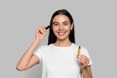 Young woman applying oil onto eyelashes on light grey background