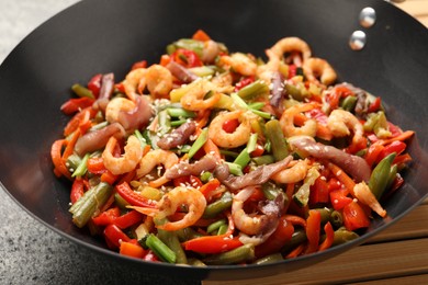 Photo of Shrimp stir fry with vegetables in wok on grey table, closeup