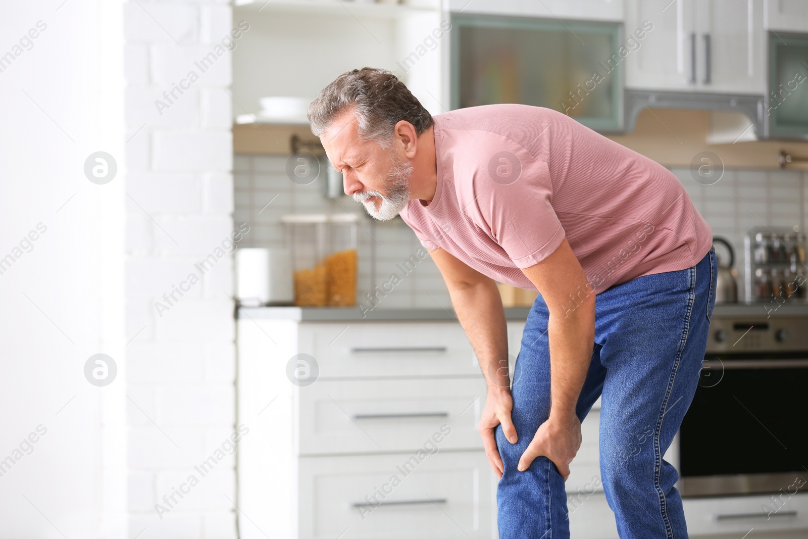 Photo of Senior man suffering from knee pain in kitchen. Space for text