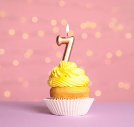 Birthday cupcake with number seven candle on table against festive lights