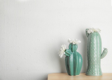 Trendy cactus shaped vases with flowers on table against light wall. Creative decor