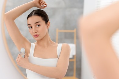 Photo of Beautiful woman applying deodorant near mirror in bathroom