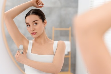 Beautiful woman applying deodorant near mirror in bathroom