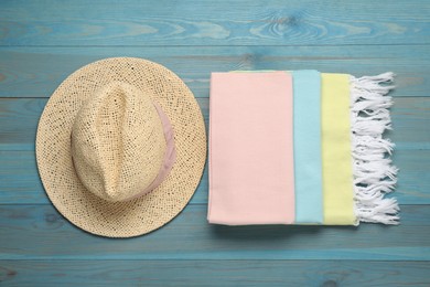 Beach towel and straw hat on light blue wooden background, flat lay