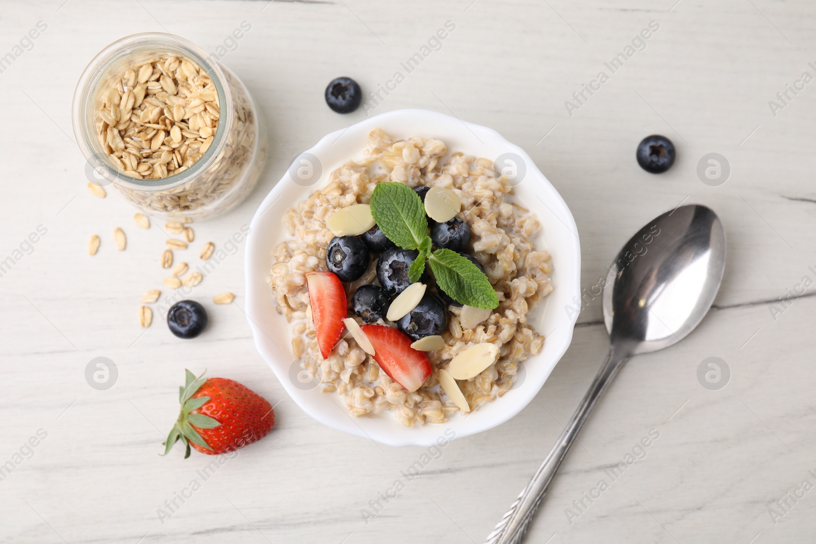 Photo of Tasty oatmeal with strawberries, blueberries and almond petals in bowl served on white wooden table, flat lay