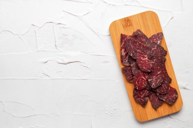 Photo of Pieces of delicious beef jerky on white textured table, top view. Space for text