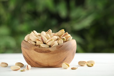 Tasty pistachios in bowl on white table against blurred background. Space for text