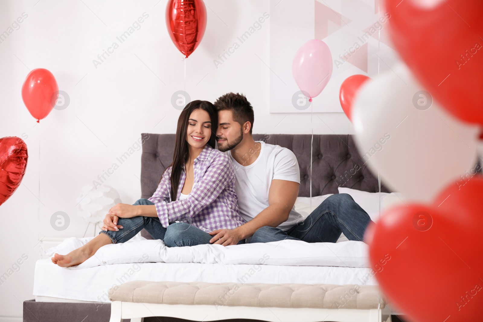 Photo of Lovely young couple in bedroom decorated with heart shaped balloons. Valentine's day celebration