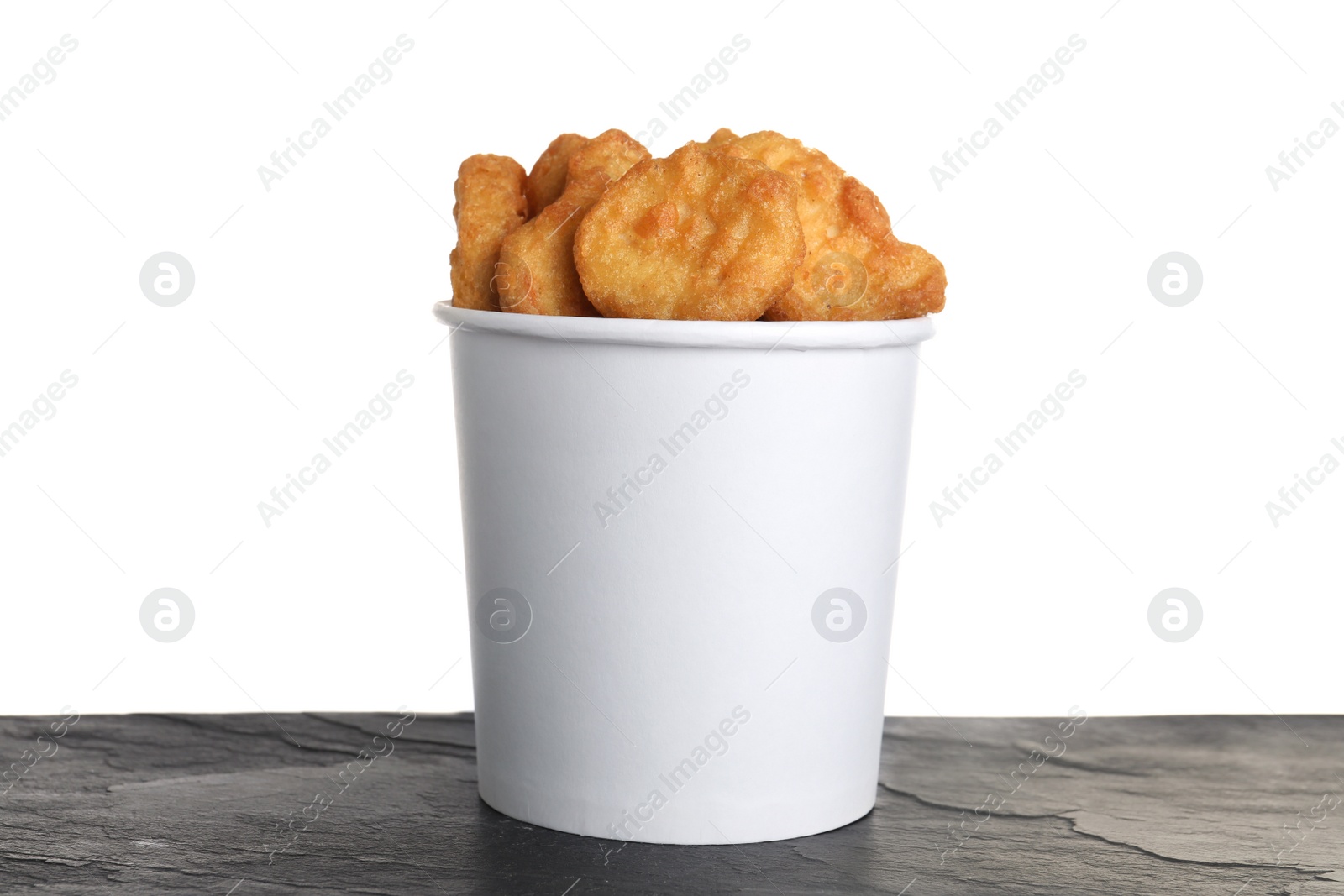 Photo of Bucket with tasty chicken nuggets on black table against white background