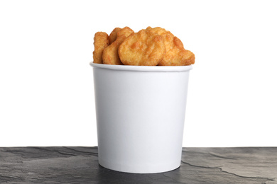 Bucket with tasty chicken nuggets on black table against white background