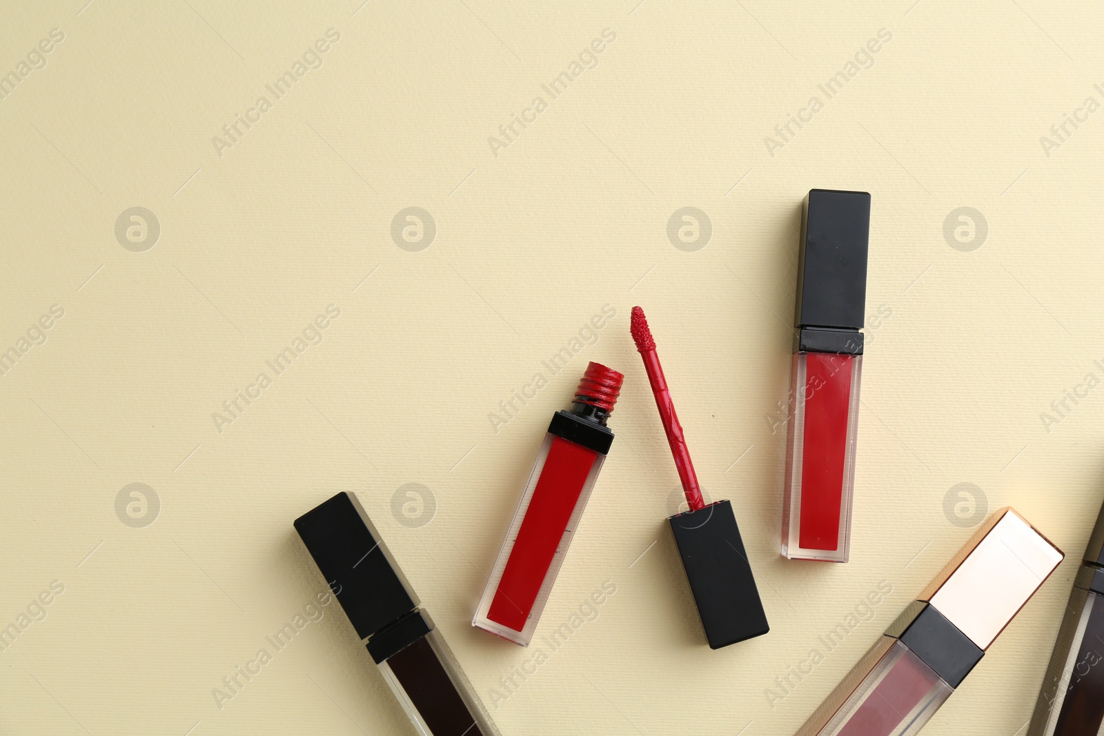 Photo of Different lip glosses and applicator on pale yellow background, flat lay. Space for text