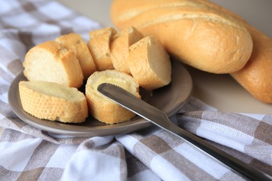 Photo of Whole and cut baguettes with fresh butter on checkered tablecloth, closeup