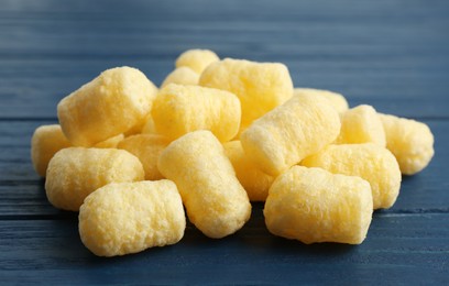 Photo of Pile of delicious crispy corn sticks on blue wooden table, closeup