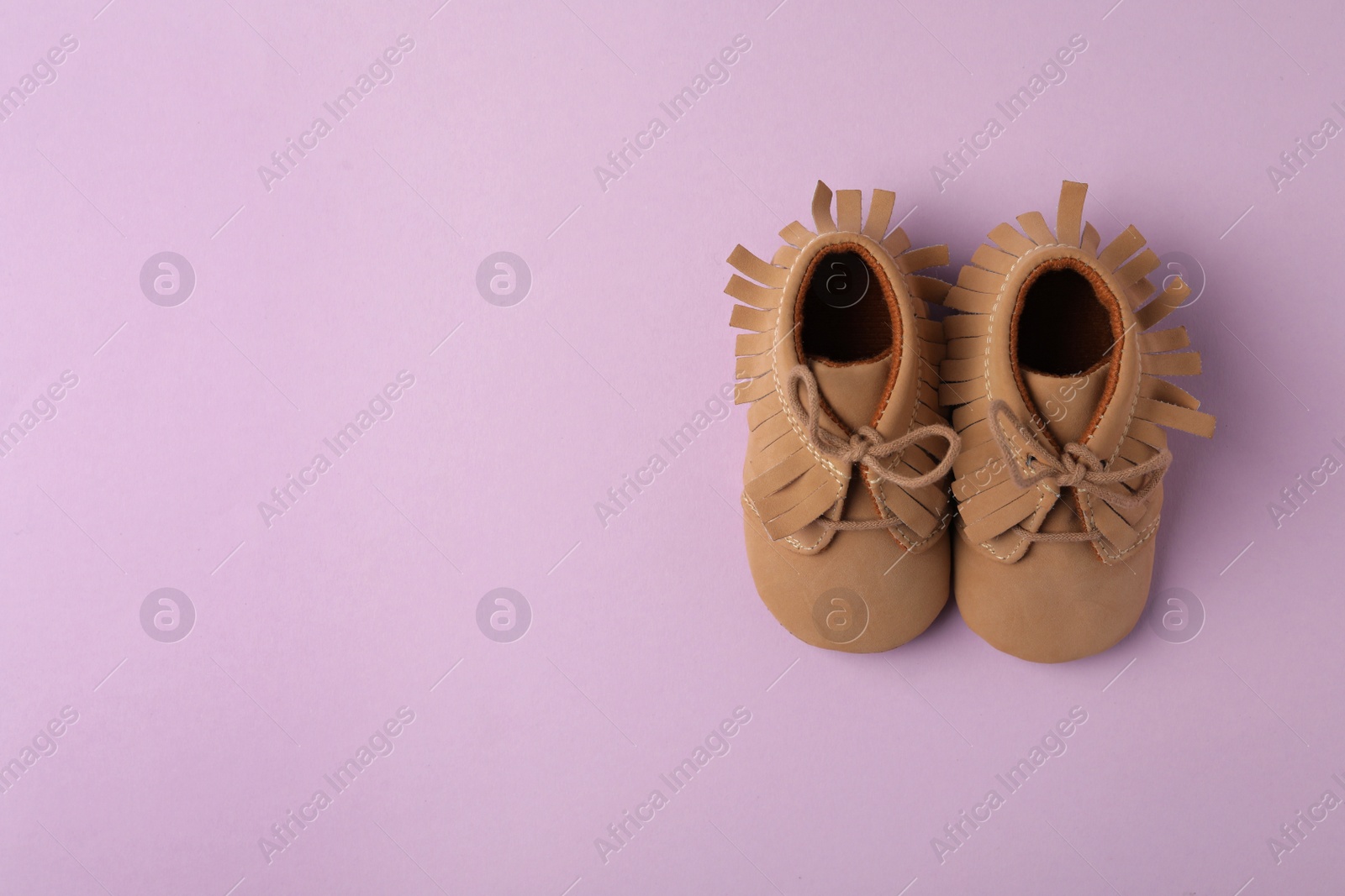 Photo of Child's booties on violet background, flat lay with space for text