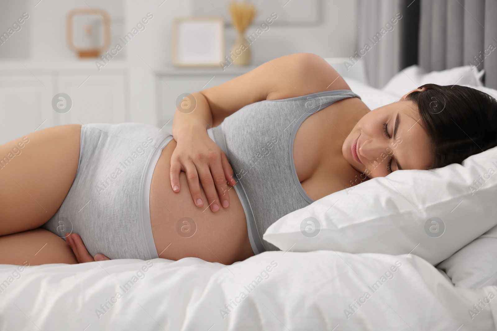Photo of Beautiful pregnant woman in comfortable maternity underwear lying on bed at home