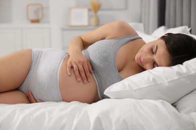 Beautiful pregnant woman in comfortable maternity underwear lying on bed at home