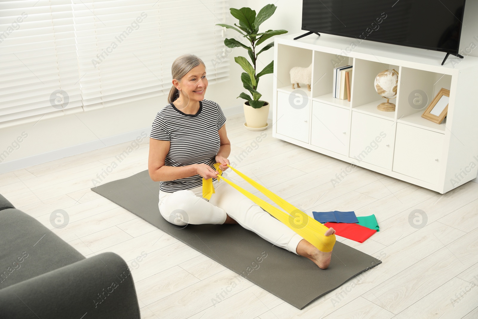 Photo of Senior woman doing exercise with fitness elastic band on mat at home