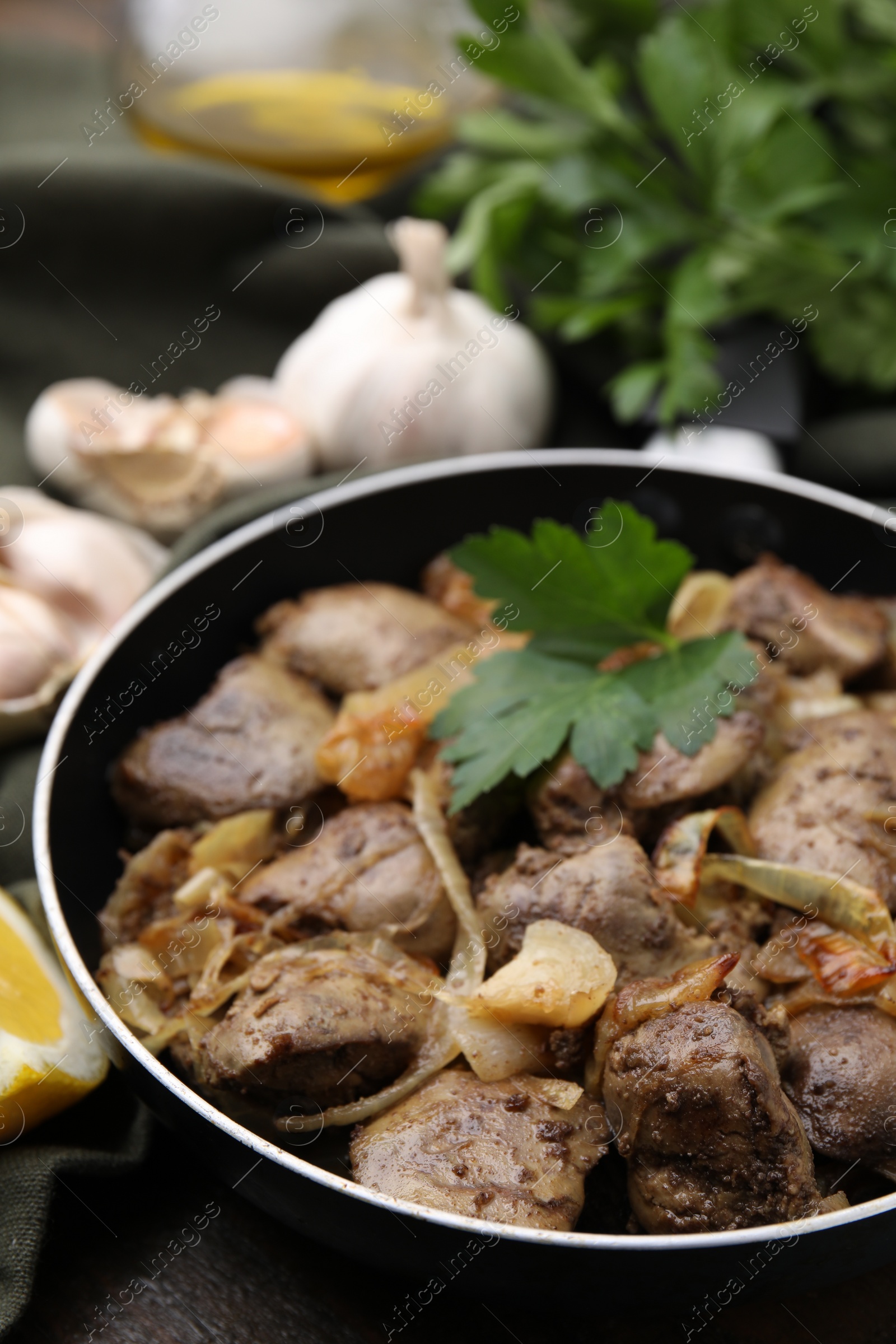 Photo of Tasty fried chicken liver with parsley and onion on table, closeup