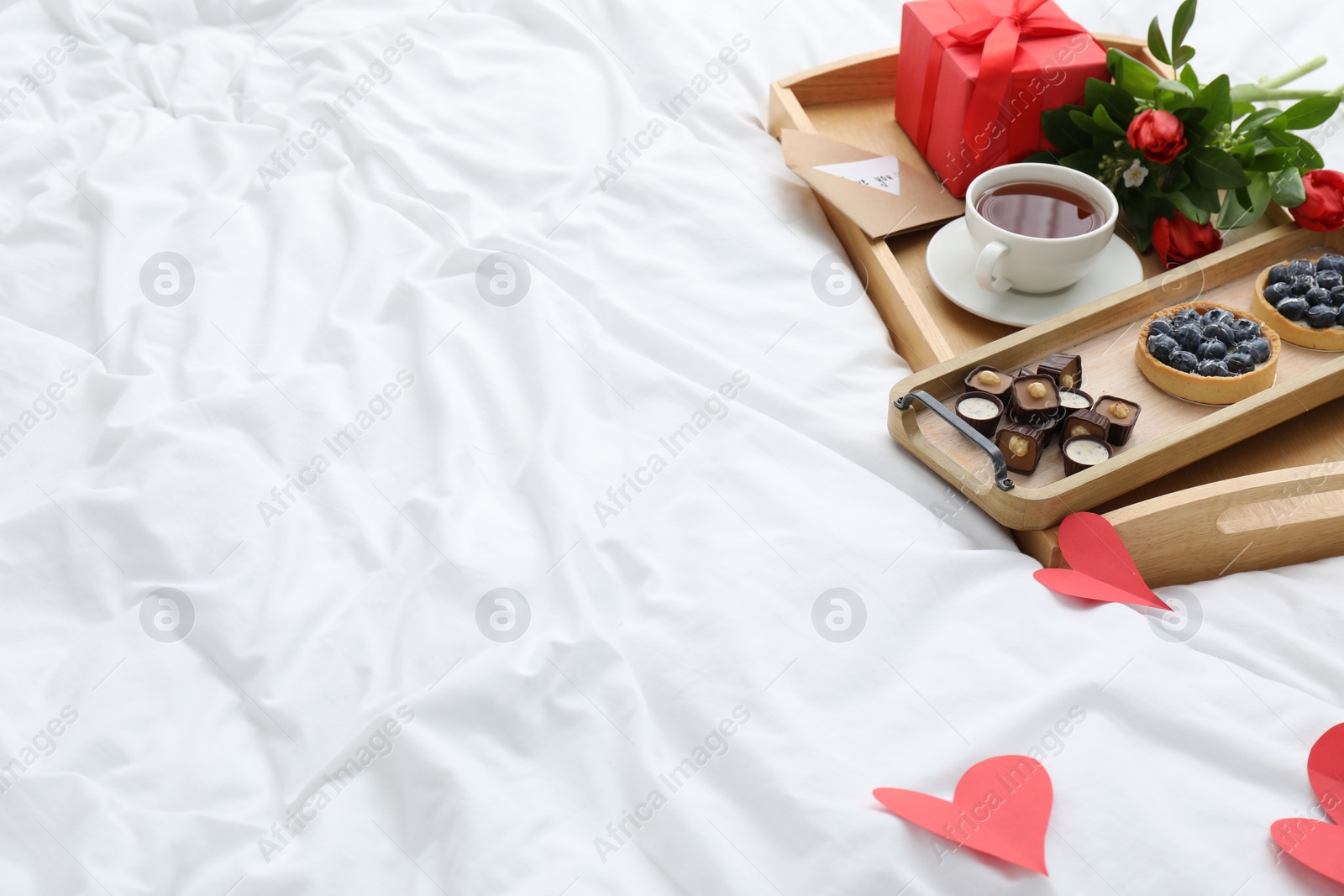 Photo of Tasty breakfast served in bed. Delicious desserts, tea, flowers and gift box on tray, space for text