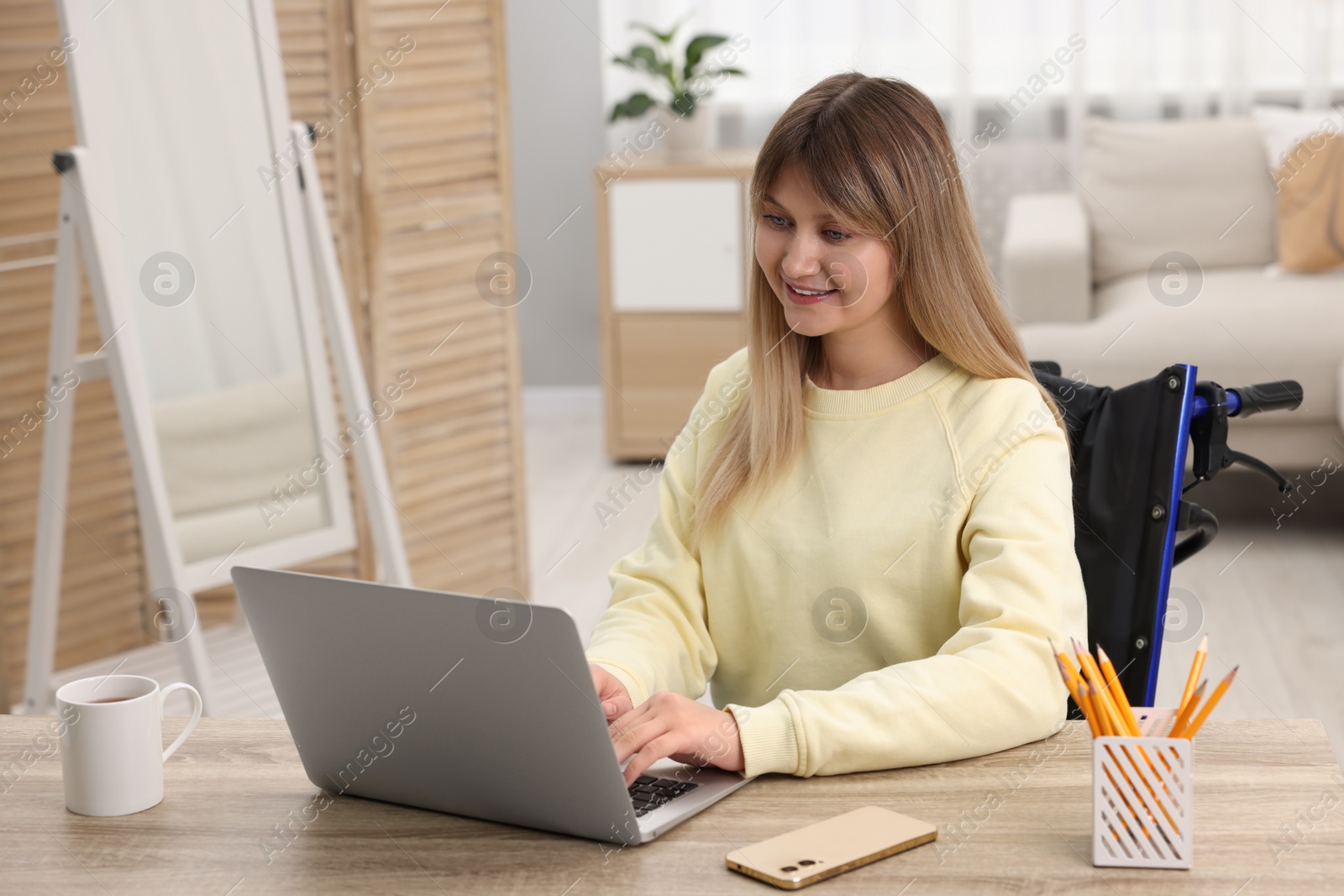 Photo of Woman in wheelchair using laptop at table in home office