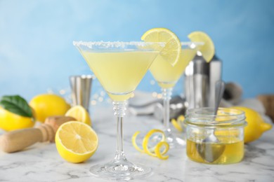 Photo of Delicious bee's knees cocktails and ingredients on white marble table against light blue background