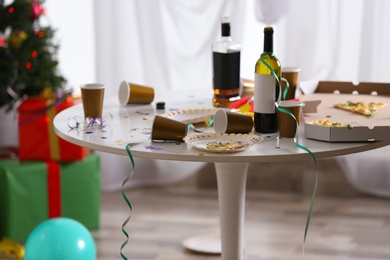 Photo of Messy table with cups, bottles and pizza indoors. Chaos after party