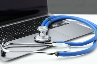 Photo of Stethoscope and modern laptop on white table, closeup