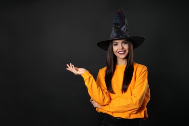 Photo of Beautiful woman wearing witch costume for Halloween party on black background, space for text