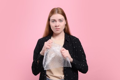 Photo of Angry woman popping bubble wrap on pink background. Stress relief