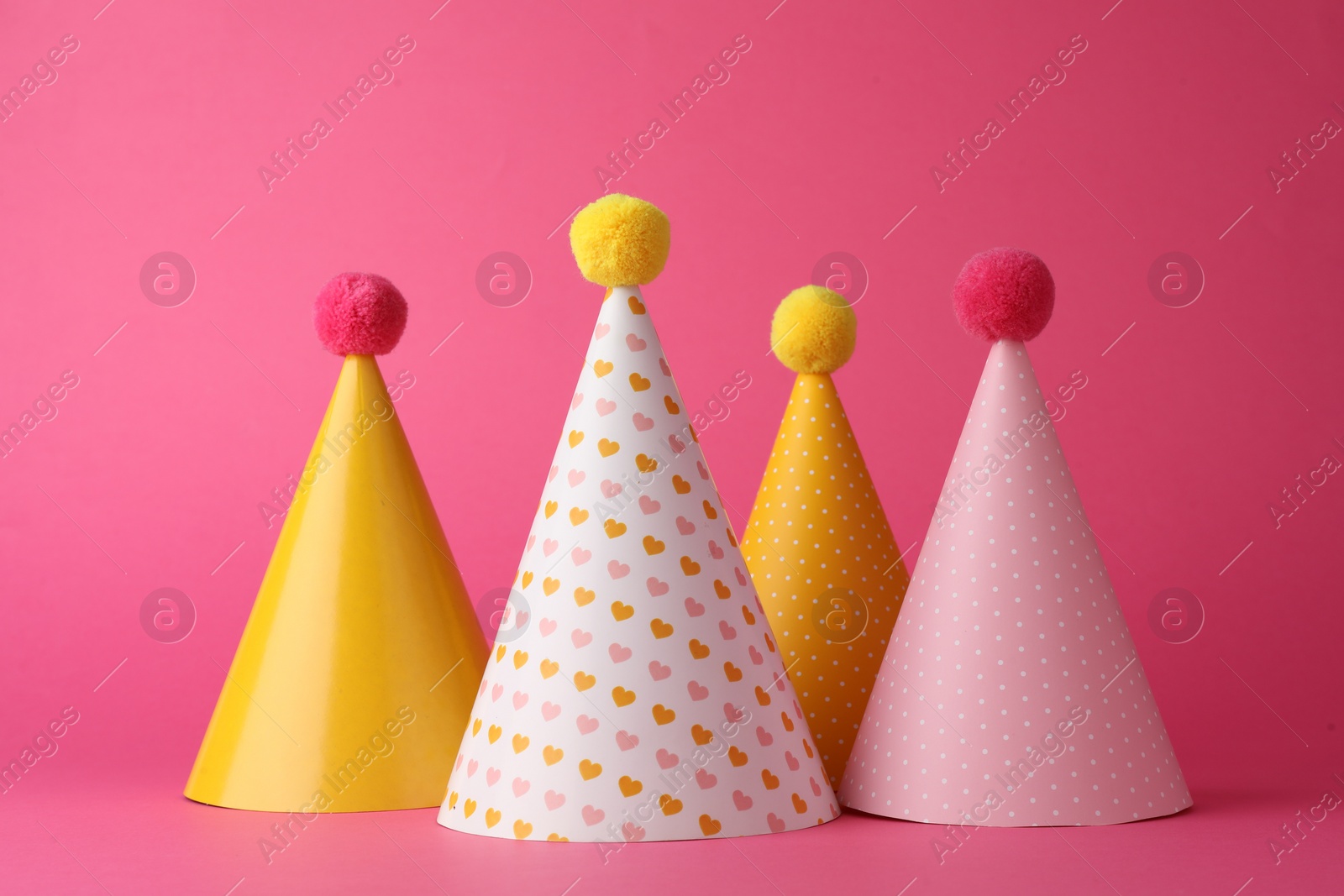 Photo of Beautiful party hats with pompoms on pink background