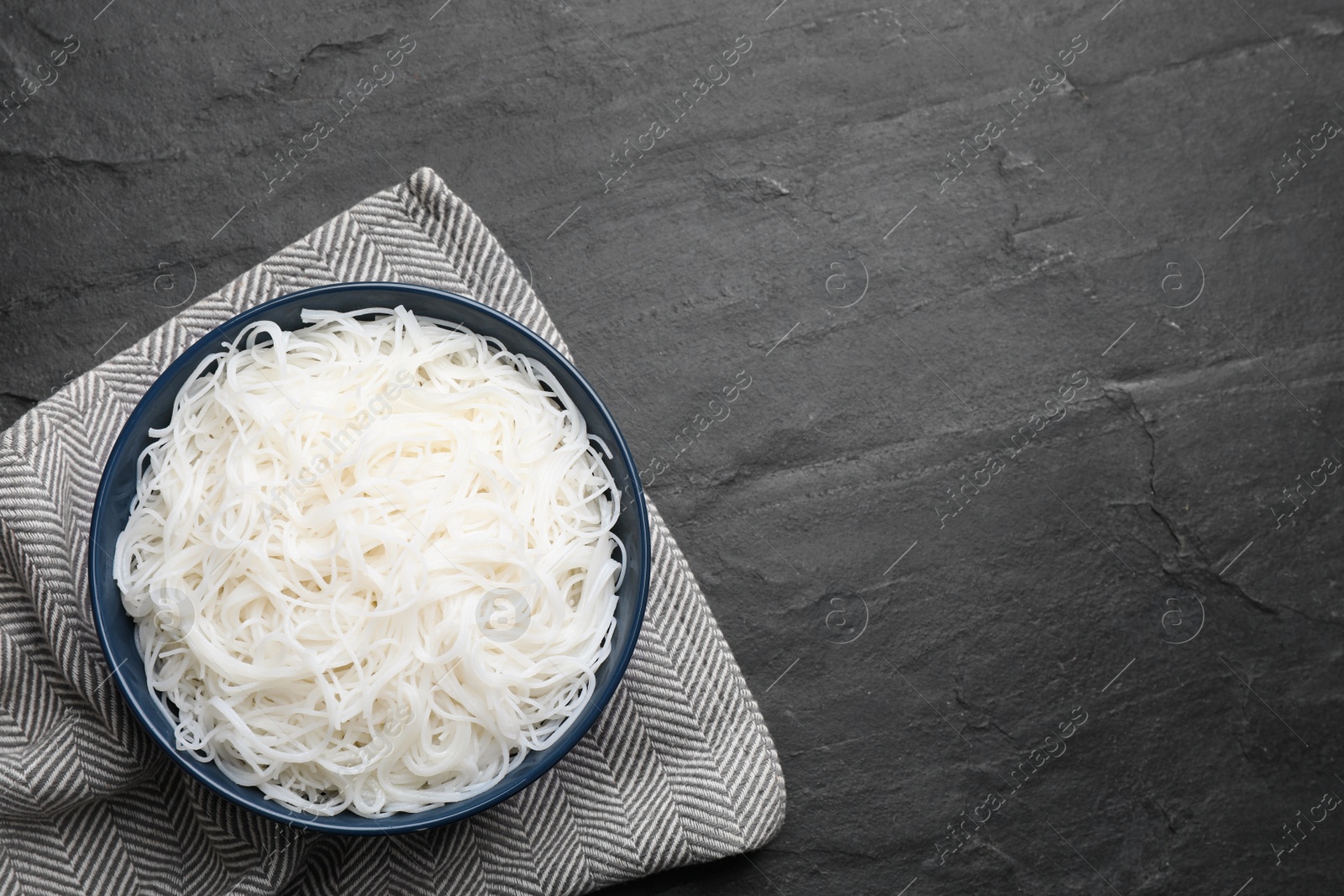 Photo of Bowl with cooked rice noodles on black table, top view. Space for text