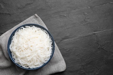 Bowl with cooked rice noodles on black table, top view. Space for text