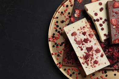 Different chocolate bars with freeze dried fruits on black table, top view. Space for text