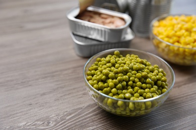Photo of Glass bowl of canned green peas on wooden table, space for text