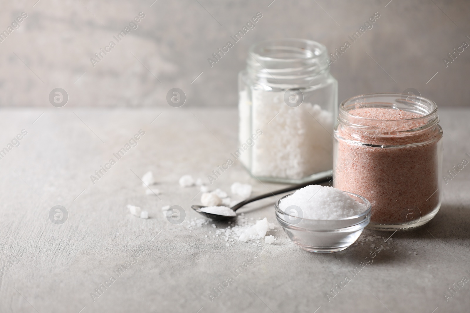 Photo of Different natural salt on grey textured table, space for text