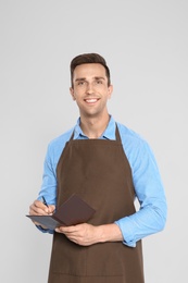 Photo of Handsome waiter in apron taking order on light background
