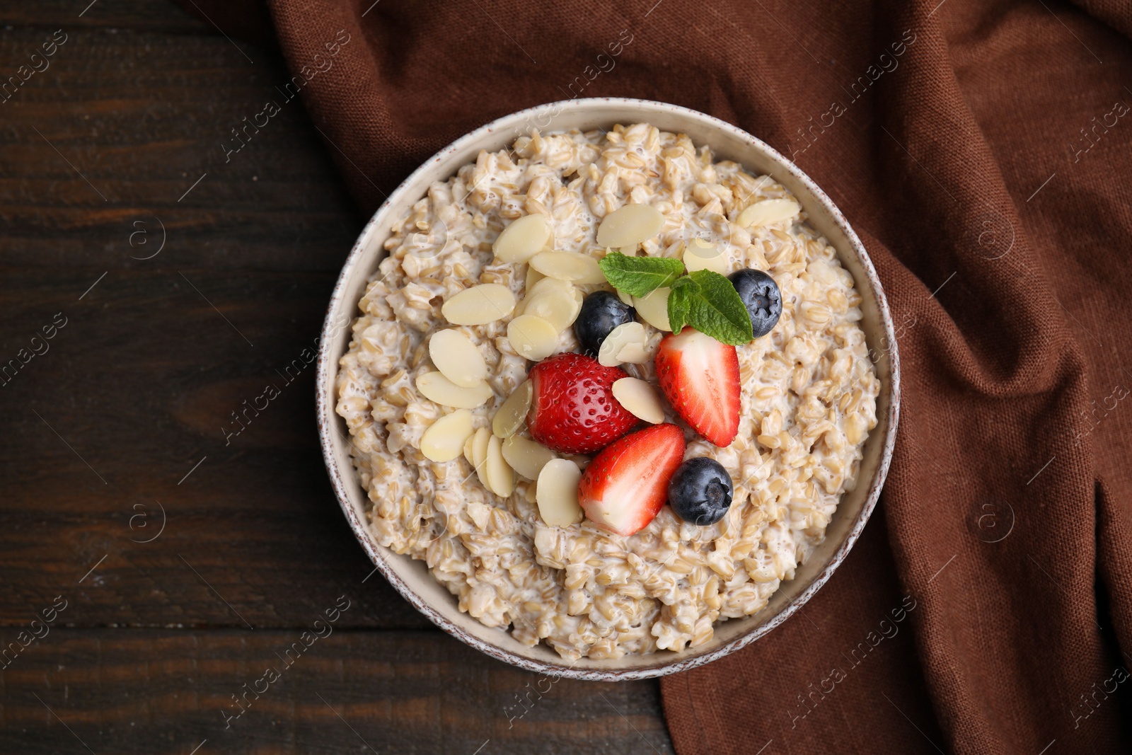 Photo of Tasty oatmeal with strawberries, blueberries and almond flakes in bowl on wooden table, top view