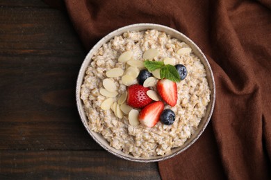 Photo of Tasty oatmeal with strawberries, blueberries and almond flakes in bowl on wooden table, top view