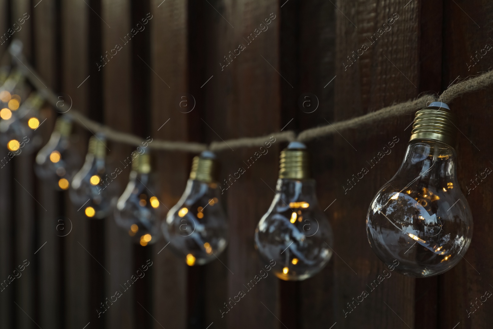 Photo of Garland of lamp bulbs hanging on wooden wall. String lights