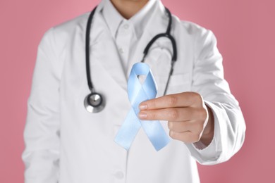 Photo of International Psoriasis Day. Doctor with light blue ribbon as symbol of support on pink background, closeup