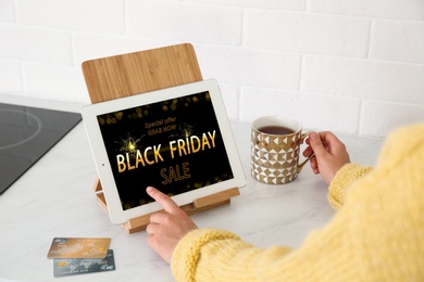Photo of Woman using tablet with Black Friday announcement at kitchen counter, closeup