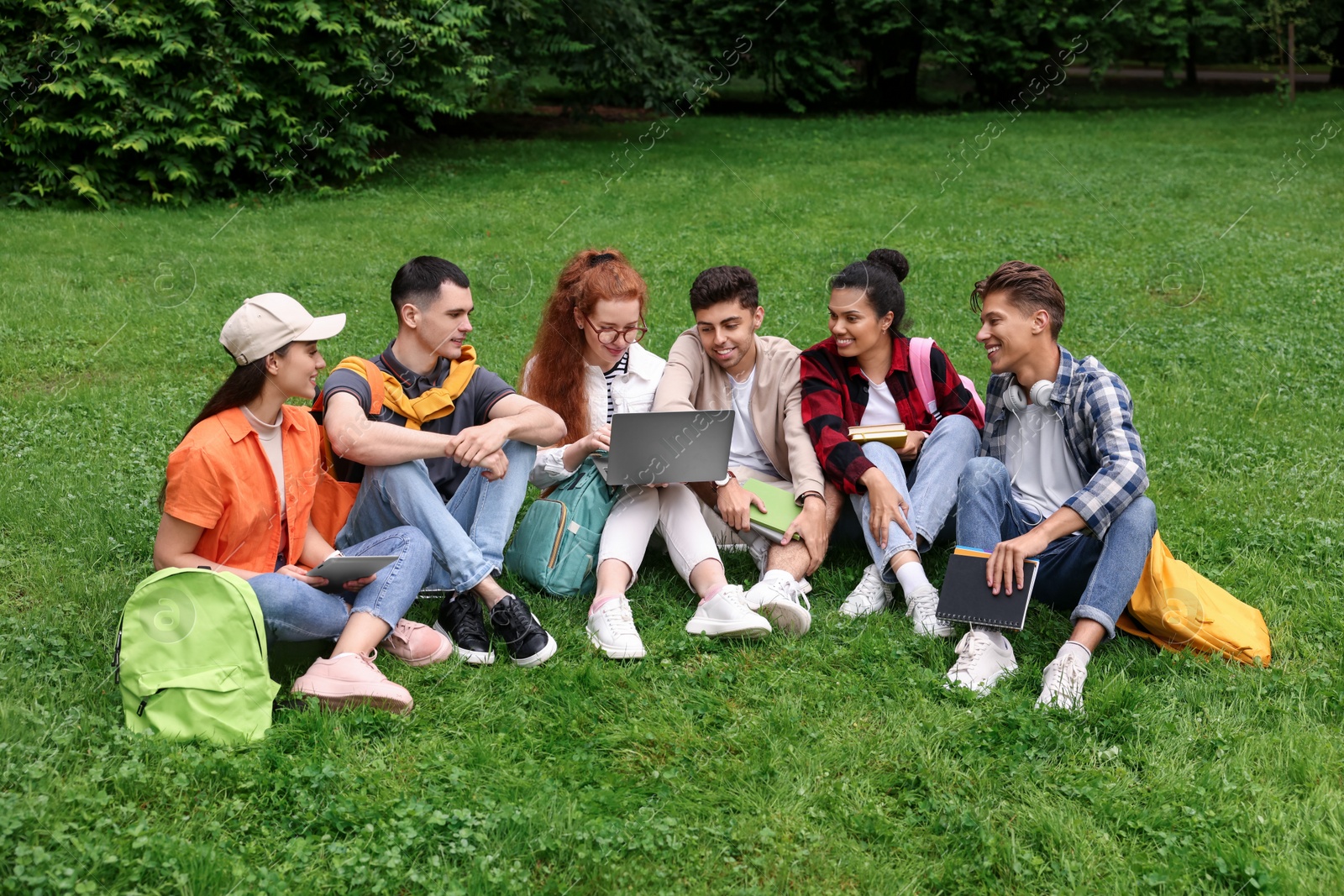 Photo of Group of happy young students learning together on green grass in park