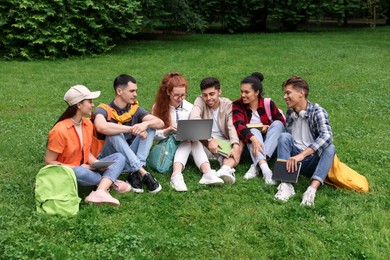 Group of happy young students learning together on green grass in park