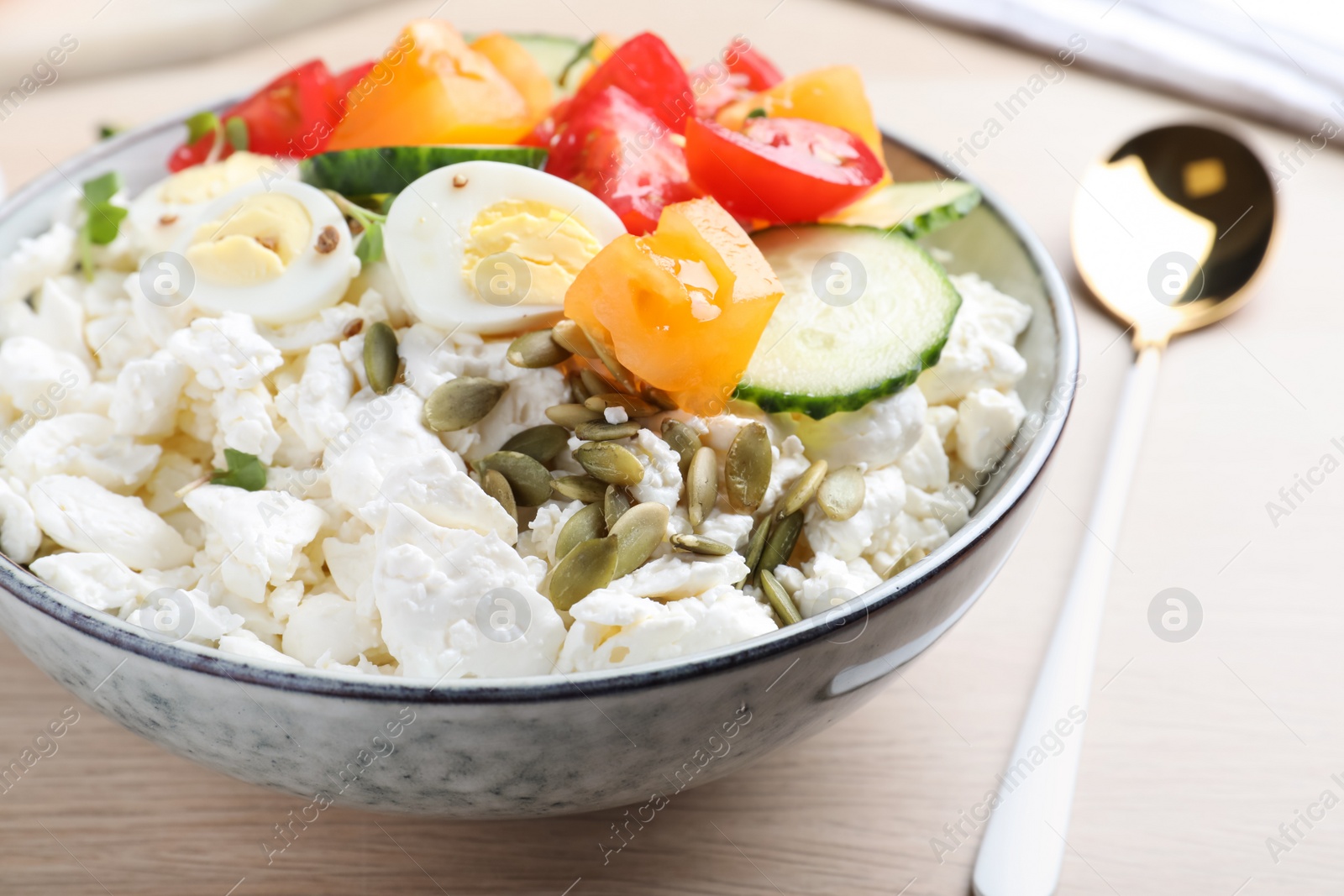 Photo of Fresh cottage cheese with vegetables, seeds and eggs in bowl on wooden table, closeup
